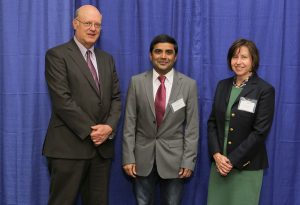 At the 2016 Penn State College of Medicine Innovation Awards, Dr. Raghavendra Gowda was named the 2016 Investigator to Watch. Gowda is pictured with A. Craig Hillemeier, MD, dean of Penn State College of Medicine and CEO of Penn State Health, and Leslie Parent, MD, vice dean for research and graduate studies for the College. The three are pictured with Gowda in the center, standing in front of a blue photo backdrop.