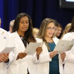 Four students in white coats are seen reciting a pledge at the 2016 White Coat Ceremony.
