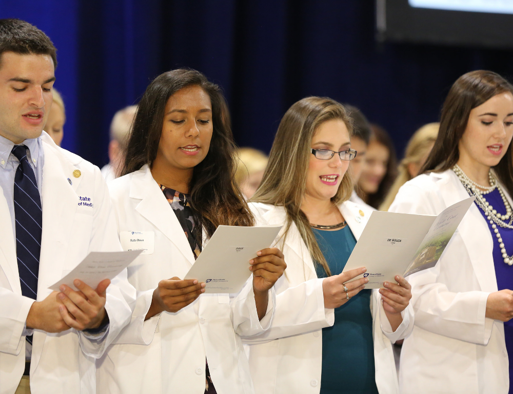 Four students in white coats are seen reciting a pledge at the 2016 White Coat Ceremony.