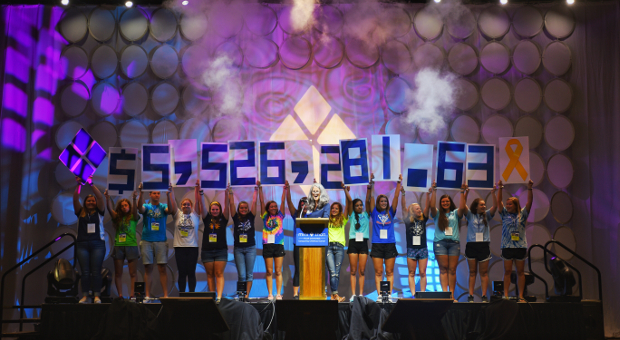 Students stand on stage holding up placards spelling out $5,526,281.63, indicating the amount of money raised through the Four Diamonds Mini-THON in 2016.