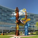 The exterior of the Penn State Health Children's Hospital is shown in the background, with a large abstract sculpture in focus in the foreground.