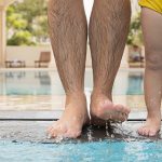 The hairy legs of a man are next to a small child's at the edge of the pool.
