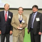 Ian Zagon, PhD, center, from the Department of Neural and Behavioral Sciences at Penn State College of Medicine, was the 2015 Innovator of the Year. The 2016 Innovation Awards ceremony will be Oct. 27, 2016. Three men are pictured; the men at left and right are wearing dark suits, and the man in the center is wearing a tan suit and holding a trophy, while smiling.
