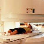A young boy lays on a platform awaiting an imaging test; a medical professional is closeby.