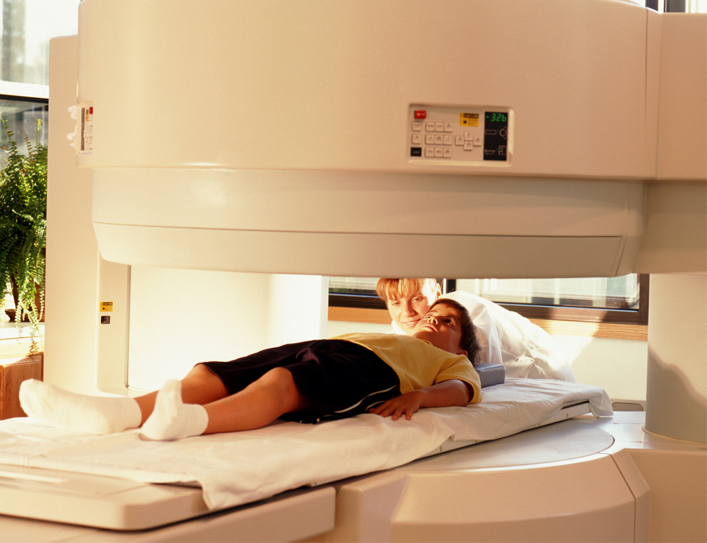 A young boy lays on a platform awaiting an imaging test; a medical professional is closeby.