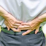 Close up of a man holding his back in pain, isolated on white background.