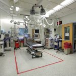 A trauma bay at Hershey Medical Center. A treatment bed is seen in the center of the room. Equipment is located around the perimeter and mounted to the ceiling.