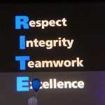 At each year's Inspired Together assembly, faculty, students and staff are honored for exemplifying the organization's RITE values of respect, integrity, teamwork and excellence. The 2016 awards assembly is pictured, with the RITE values projected onto a blue screen between the images of two Nittany Lion shields. People attending the assembly are seen in a crowd in front of the screen.
