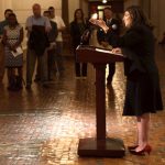 Dr. Oralia Garcia-Dominic discusses the first Pennsylvania Latino/Hispanic cancer burden report in September 2016 at the Pennsylvania State Capitol. Garcia-Dominic is pictured at right, standing at a podium and addressing a seated crowd seen at the left of the photo.