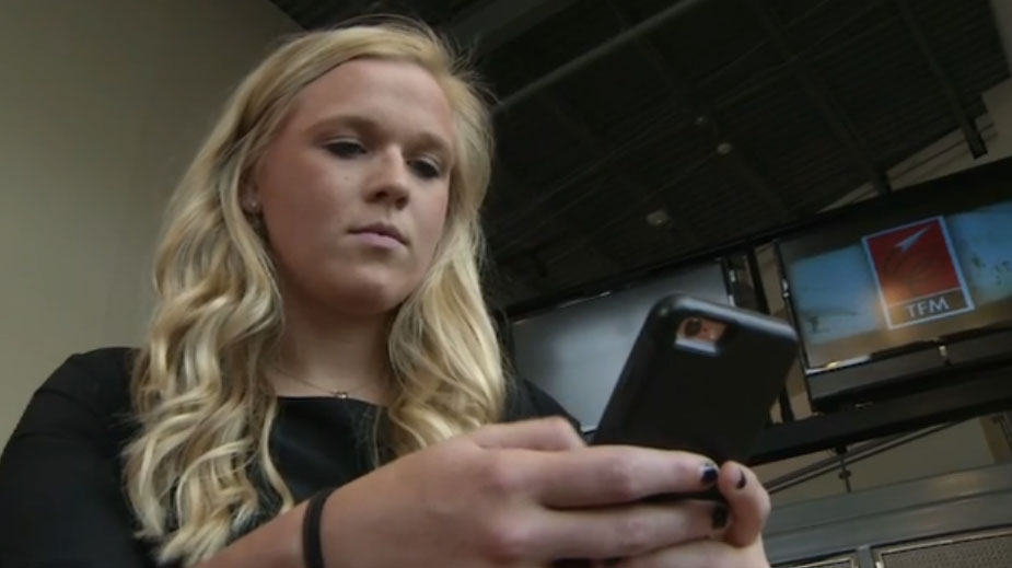 A teenage girl is seen looking at information on a black smartphone.