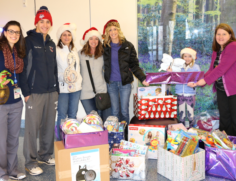 Seven people pose for a photo. In front of them are several boxes of gifts.
