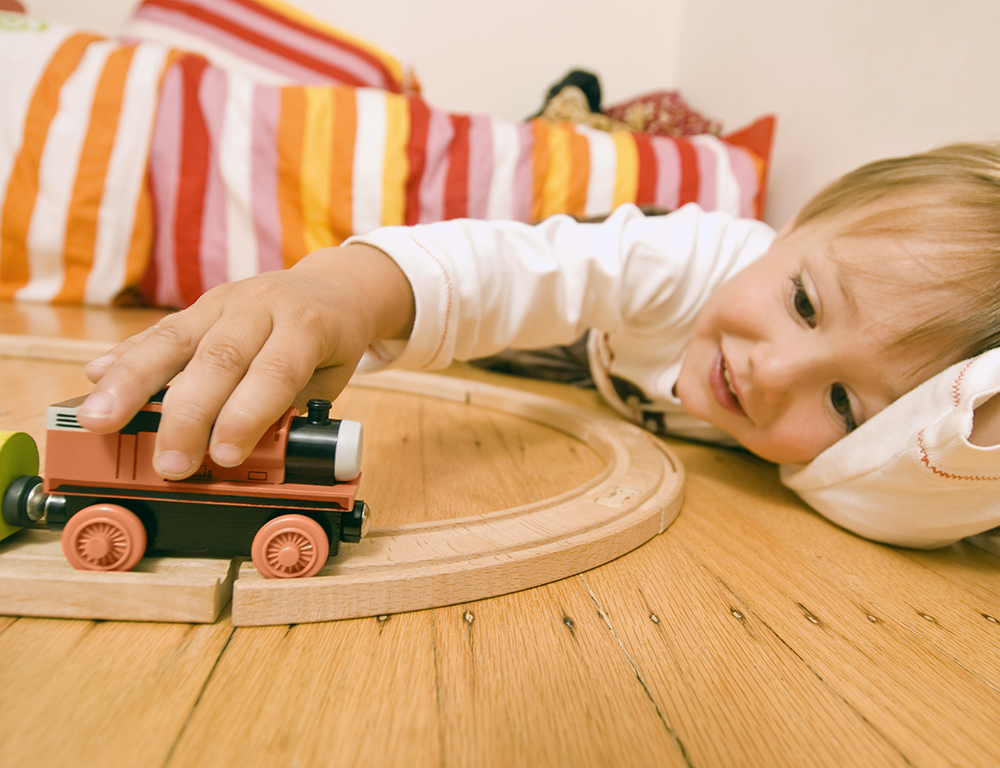 A child lays on the floor while playing with a toy train set.