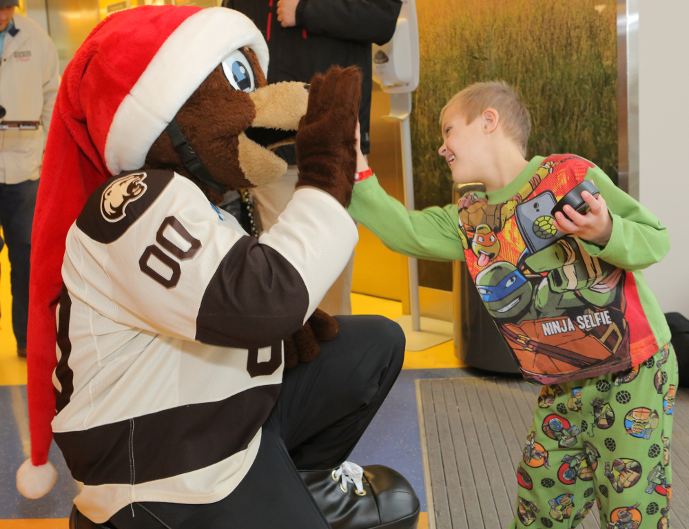 A young boy in Teenage Mutant Ninja Turtles pajamas smiles as he gives a high five to Coco, the Hershey Bears mascot.