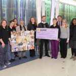 Representatives of Penn State Health Children's Hospital and Spirit Halloween stores pose in the hospital lobby with an oversized check and a collage with photos of children.