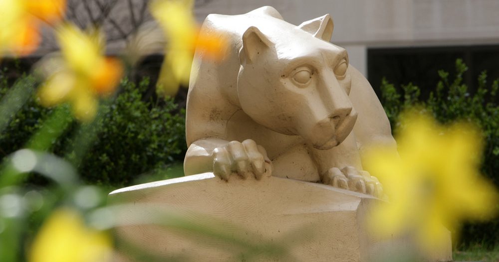 A statue of the Nittany Lion, with yellow flowers in the foreground, out of focus.