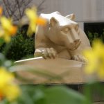 A statue of the Nittany Lion, with yellow flowers in the foreground, out of focus.