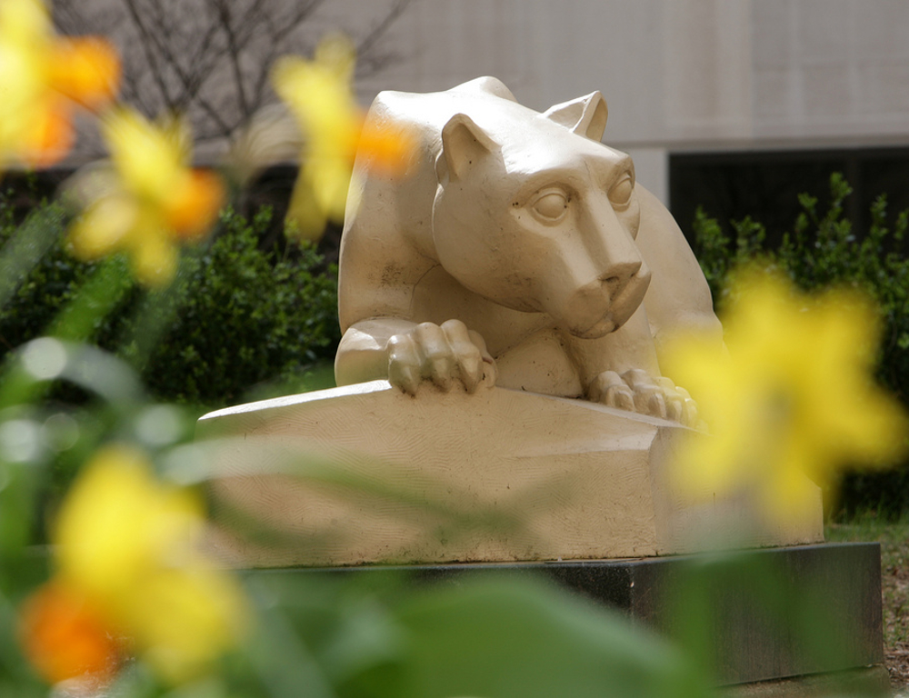 A statue of the Nittany Lion, with yellow flowers in the foreground, out of focus.