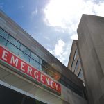 A view of an "Emergency" sign -- white letters on red background -- looking up from the ground.