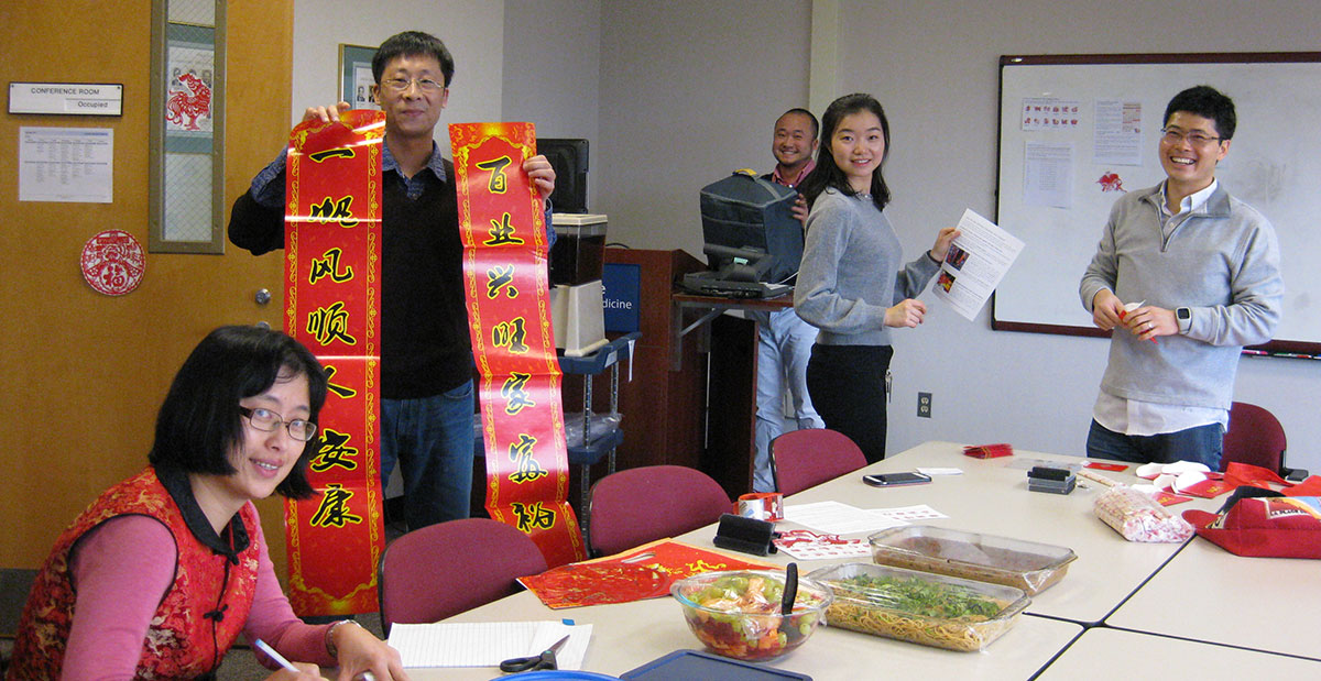 Members of Penn State College's Department of Cellular and Molecular Physiology held a celebration in honor of Chinese New Year. The holiday took place Jan. 28, 2017. Several members of the department are pictured in a conference room. One is holding a large banner with Chinese characters; others are looking at each other or the camera and smiling. Various food and other items are seen on the table in front of the group.