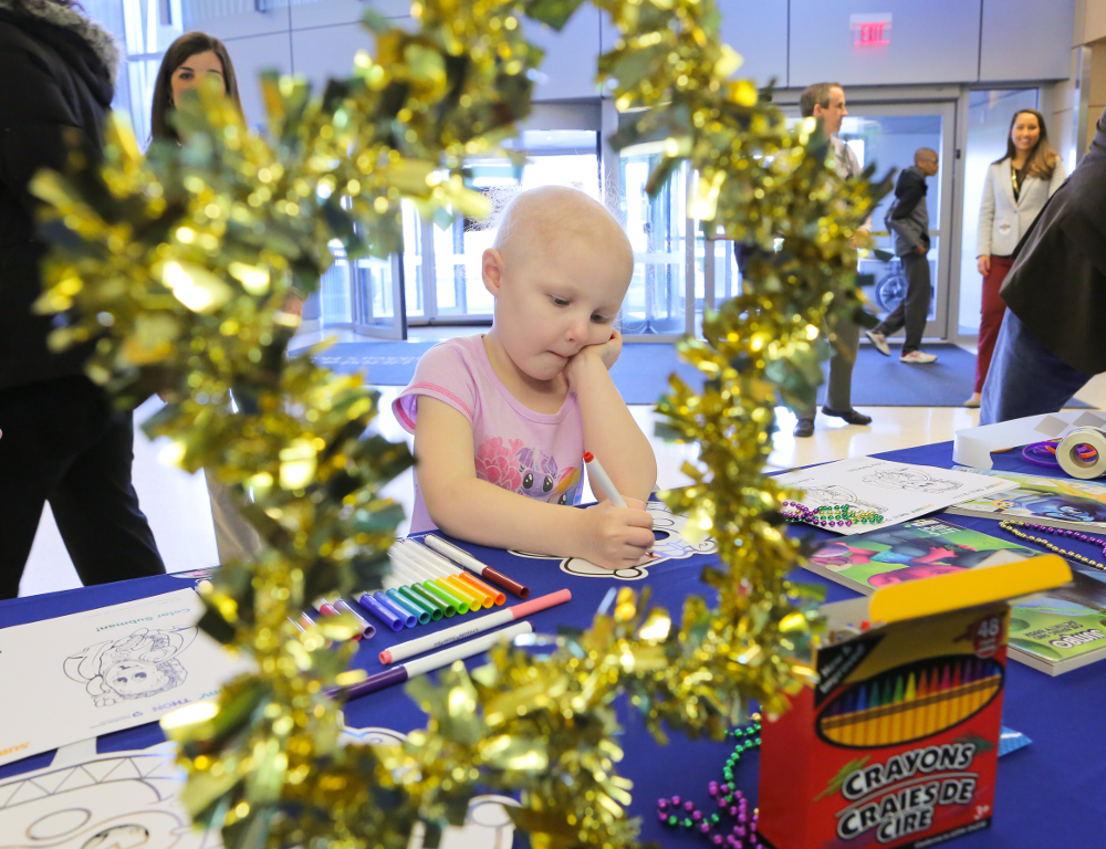 A young girl colors a mask with a magic marker. The photo is taken though the view of a star made of garland.