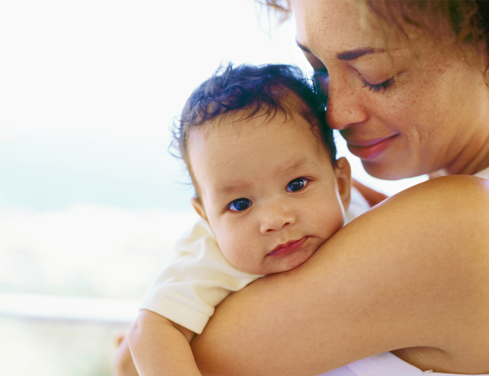 A woman holds a baby, who is looking over her shoulder into the camera. The woman is looking at the child™s head.