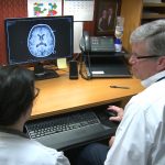 A man and a woman look at a computer screen on which a brain scan is depicted.