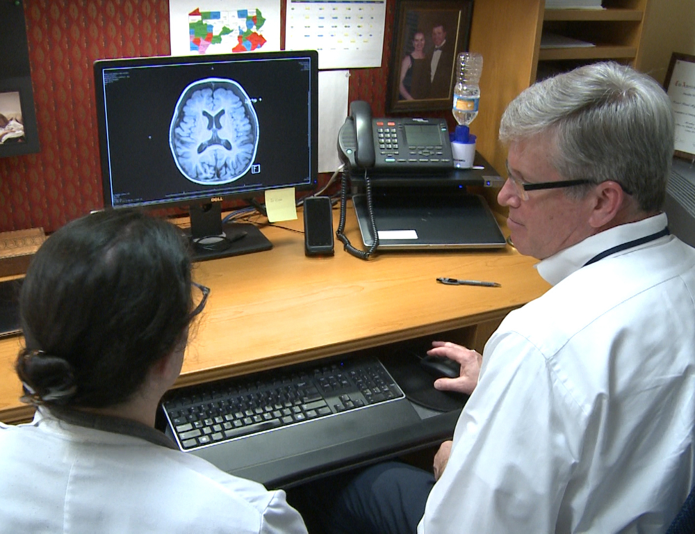 A man and a woman look at a computer screen on which a brain scan is depicted.