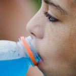 A close-up of a young girl drinking a blue sports drink.