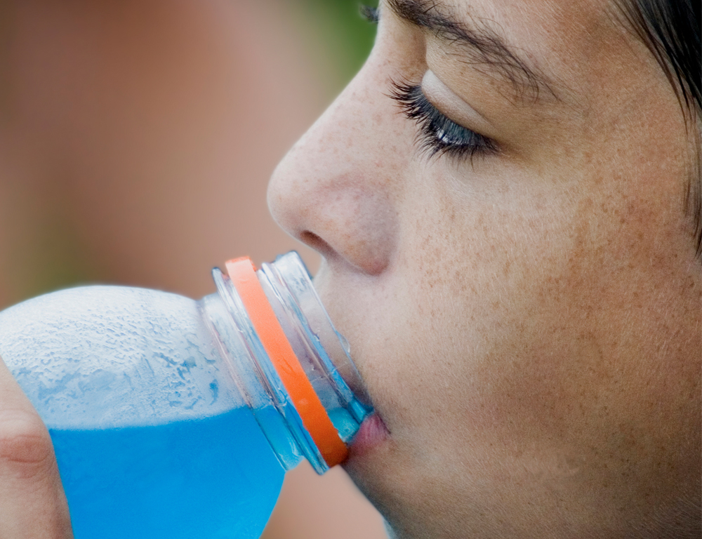 A close-up of a young girl drinking a blue sports drink.