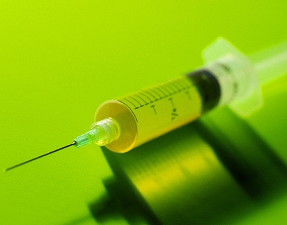 Close-up of a syringe filled with liquid, on a bright green background.