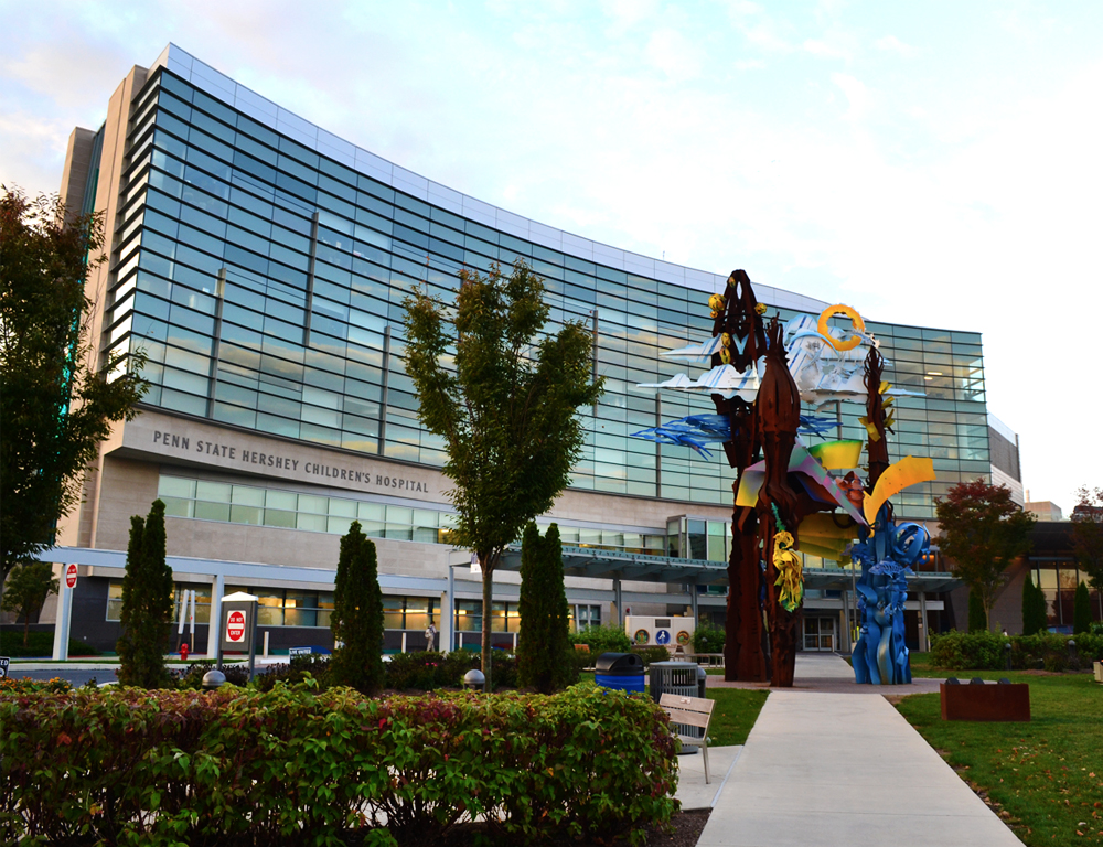 External view of Penn State Health Children's Hospital, during the day. A multi-colored metal sculpture and some trees and bushes are in the foreground.