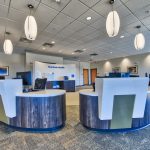 Inside the new Penn State Medical Group site in Mechanicsburg, four white pendulum lights hang down over the registration area, made up of blue desks with elevated white counters in a semicircle in the center of a room, which has the Penn State Health logo on the rear wall.