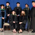The 2017 Penn State College of Medicine MD-PhD Medical Scientist Training Program graduated six students in May 2017. Pictured are, seated from left, Marie Bulathsinghala and Lauren Kaminsky; and standing, Dr. Leslie Parent, Program Co-Director, Gene Cozza, Steve Steinway, Zainul Hasanali, and Dean A. Craig Hillemeier. Not pictured is graduate Cody Weston. The graduates and two faculty members are pictured wearing full academic regalia, including hoods, gowns and mortarboards. They are in a large room with a blue photo backdrop behind them.