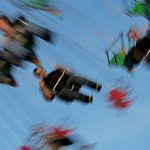 A partially sideways view of riders on an amusement park swing ride, blurry to depict motion.