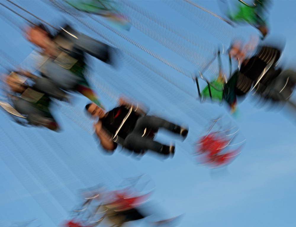 A partially sideways view of riders on an amusement park swing ride, blurry to depict motion.