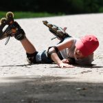 A child wearing roller blades lays on a brick driveway, apparently after falling.