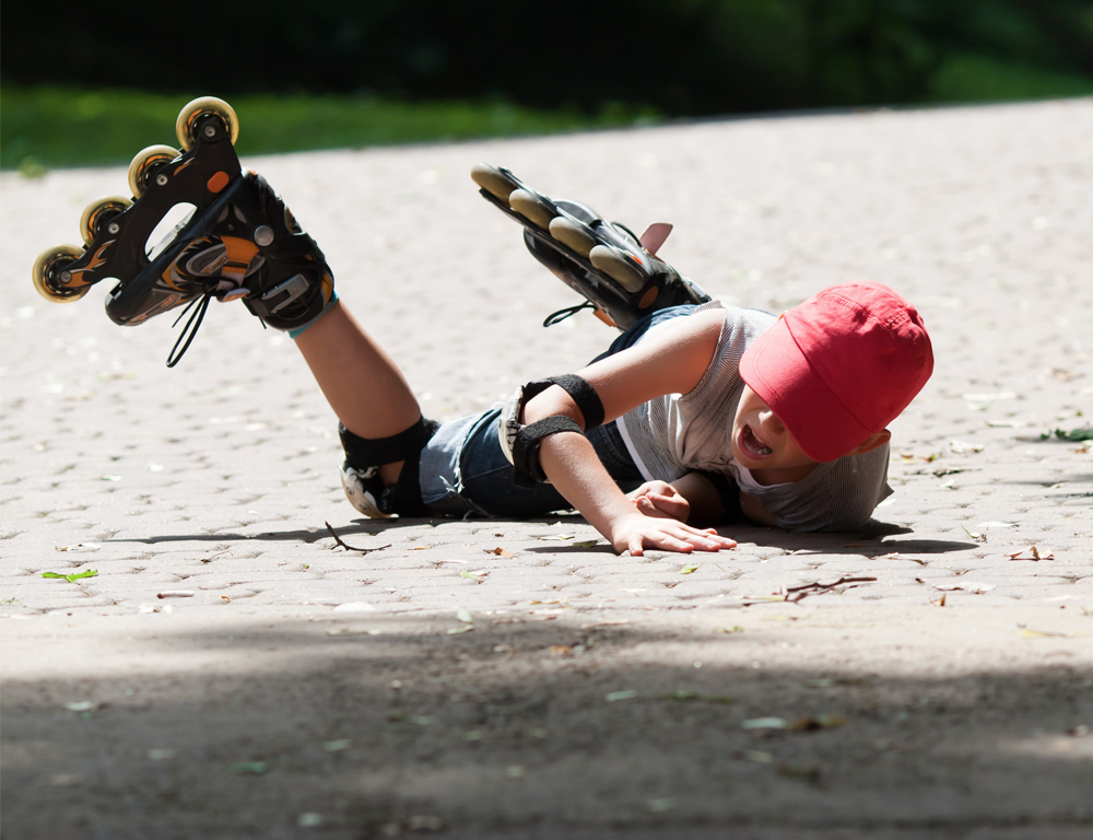 A child wearing roller blades lays on a brick driveway, apparently after falling.