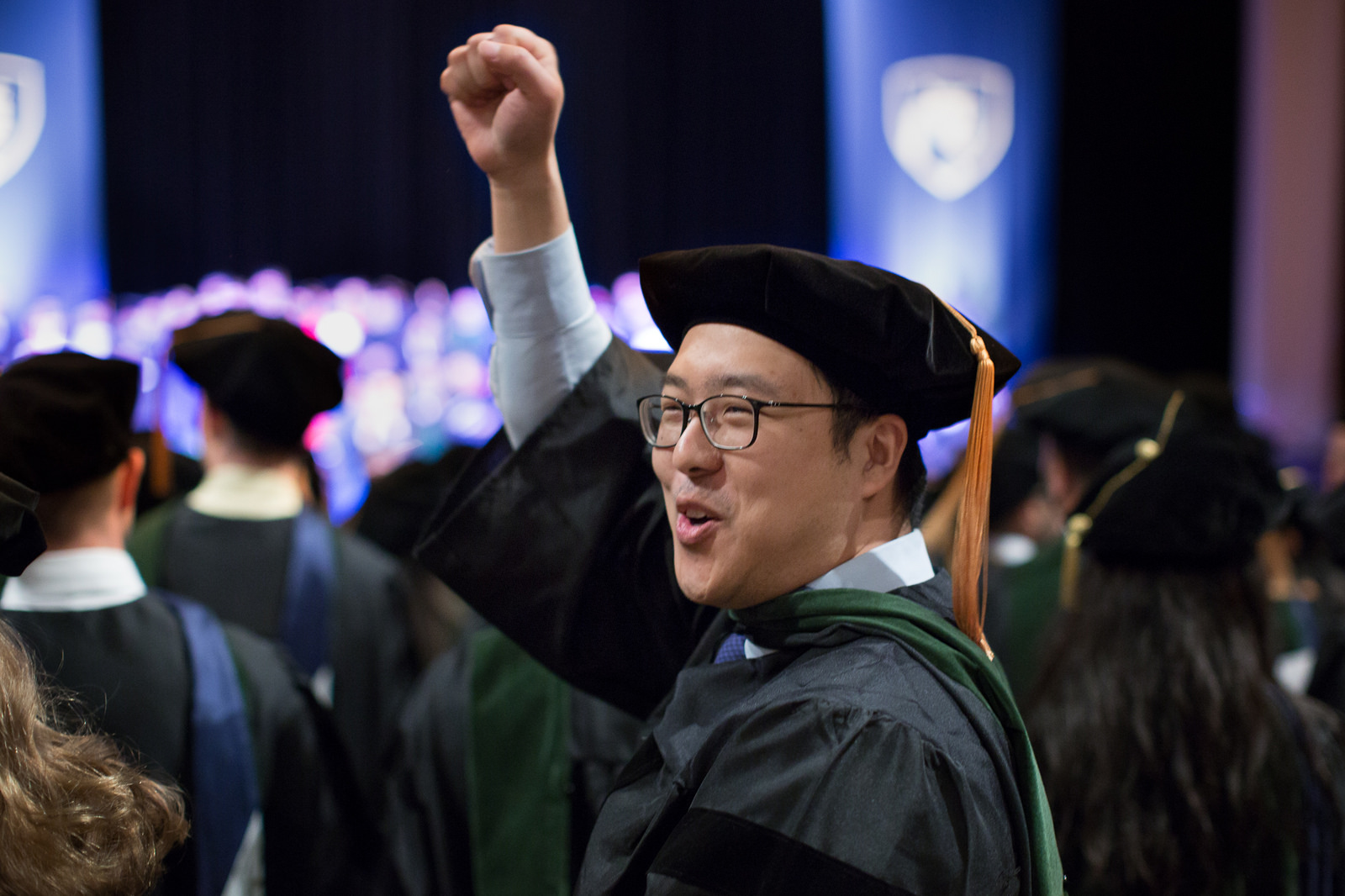 Penn State College of Medicine's Commencement was held at Founder's Hall at the Milton Hershey School on May 21, 2017. Pictured, Adrian Wang, MD, cheers during the ceremony. Wang is pictured wearing a cap and gown with his right hand extended in the air.