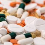 A close-up of a pile of medication, including white pills, orange pills and green and white capsules.