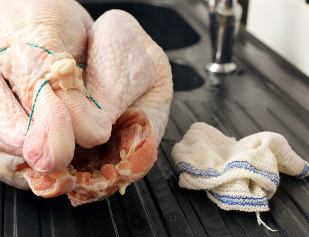 A close-up of a raw turkey and a white and blue washcloth sitting on a counter. A kitchen sink is in the near background.