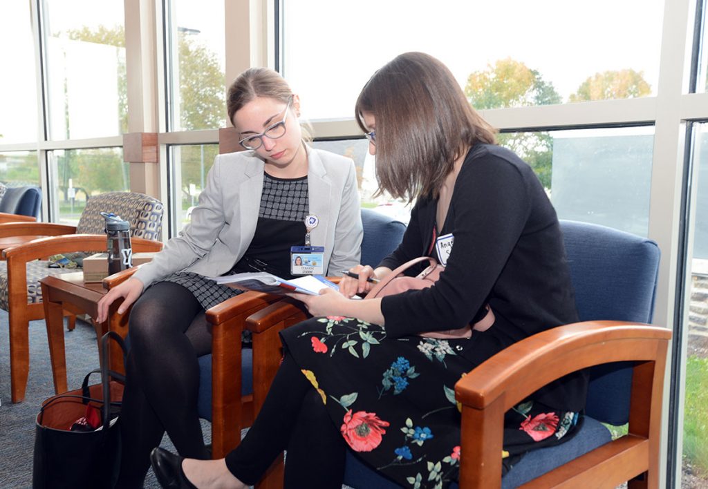Graduate students Cecilia Bove and Angela Snyder, both PhD candidates in Neuroscience, review the events of Penn State College of Medicine Career Day 2017. The two women are pictured sitting in front of a window, looking together at a book.