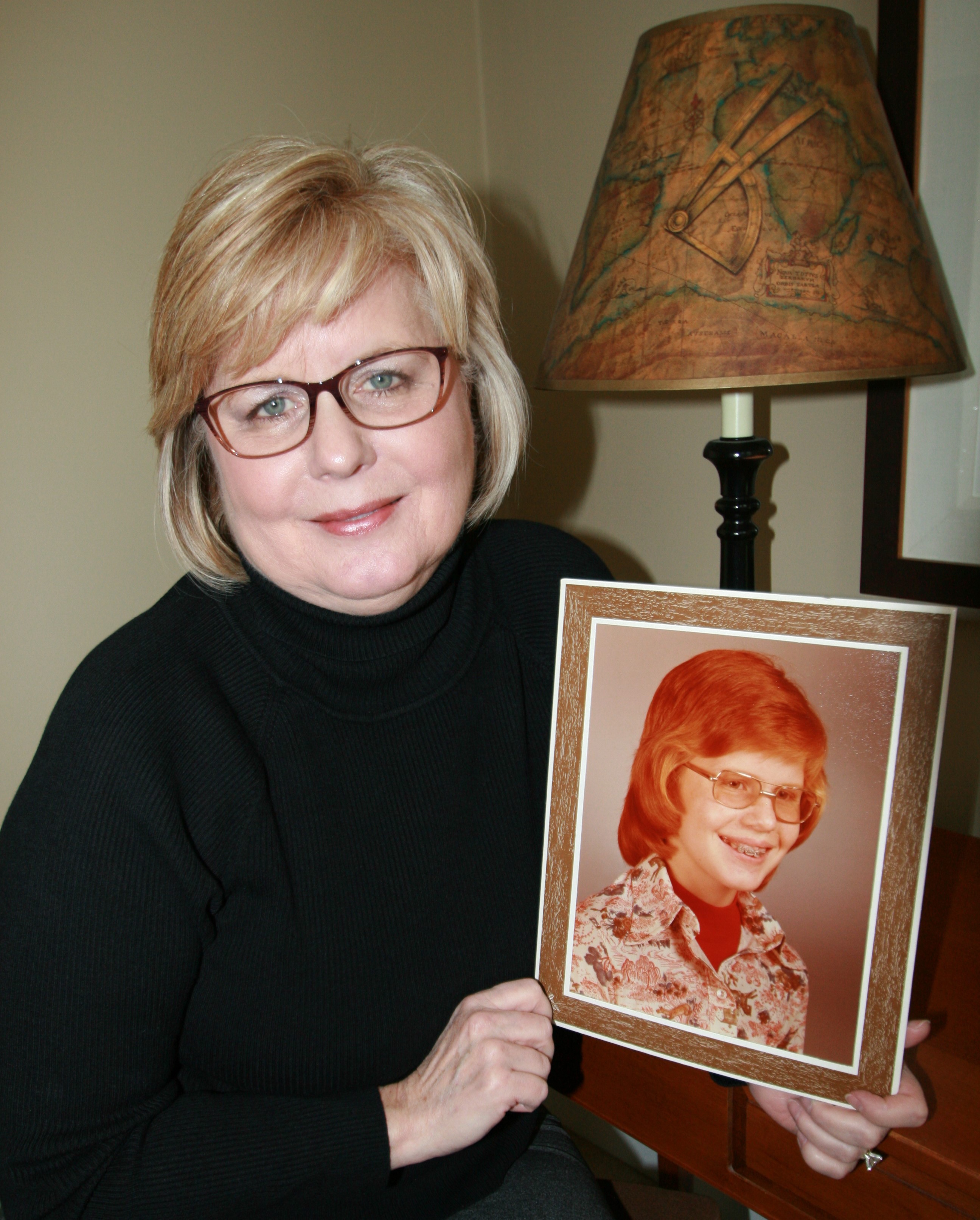 Middle-aged white woman with blonde hair and glasses holds a photo of herself in 1975.
