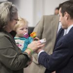 A man hands an orange and yellow rose to a woman who's holding a young child.