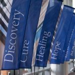 Banners inside Penn State Cancer Institute are depicted with the words Discovery, Cure, Healing and Hope visible, and other banners with unreadable text seen in the background.