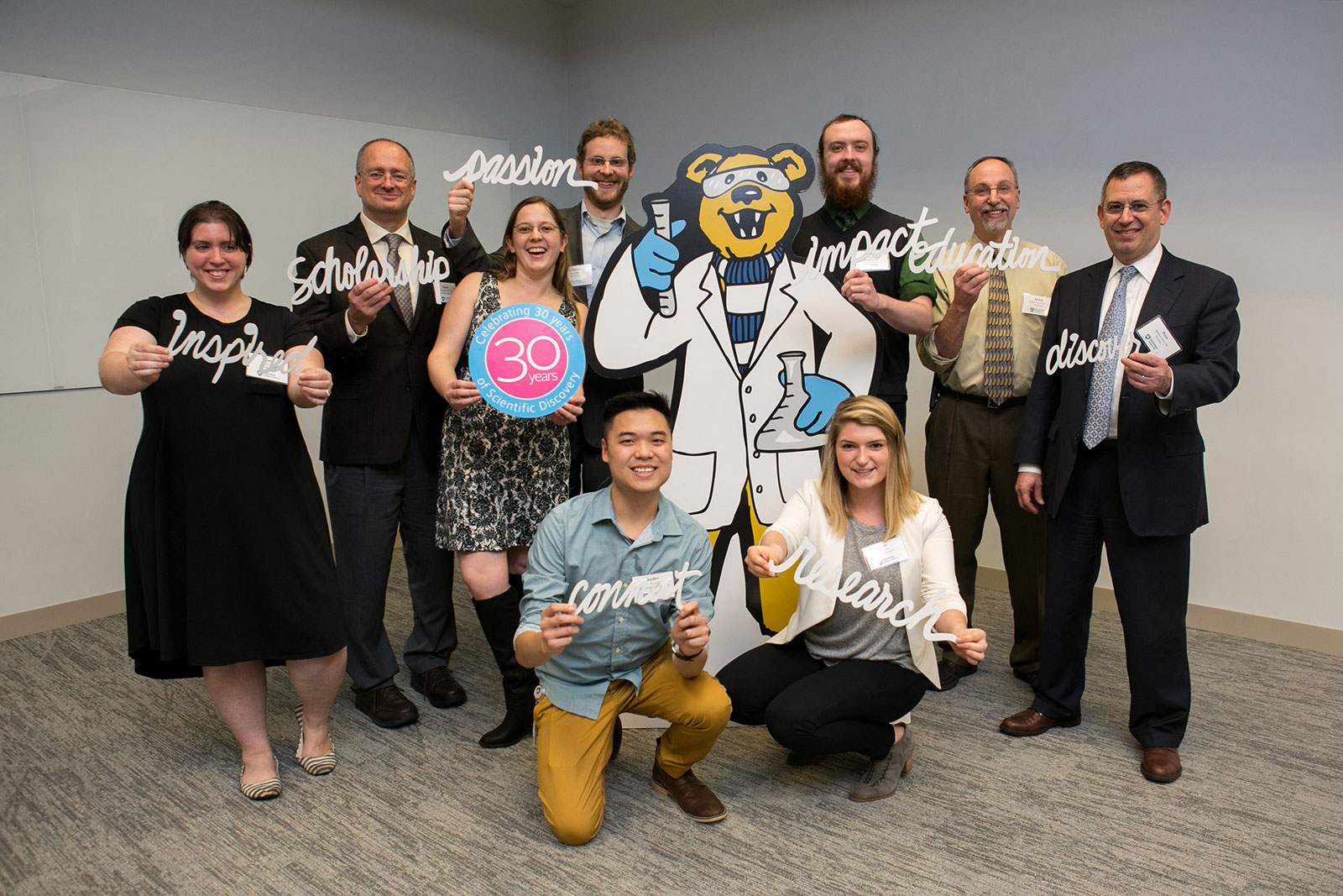 Students and alumni gather at the alumni dinner as part of the 2018 Graduate Research Forum. Pictured are, back row from left, Jesica James, Dr. David Antonetti (PhD CMBIO ™92), Jillian Weissenrieder, Dylan van Kampen, Ian Hayman, Dr. Edwin Gillman (PhD BCHEM ™90), and Peter Masiakos (MS PHSIO ™90), and in front, Jordan Chang and Emily Schleicher. The group members are seen holding 3D prints of words such as research and session, and holding the logo for the 30th anniversary forum. They are standing around a large cutout of the Penn State Nittany Lion mascot; in the cutout, the mascot is wearing a lab coat and holding a beaker.