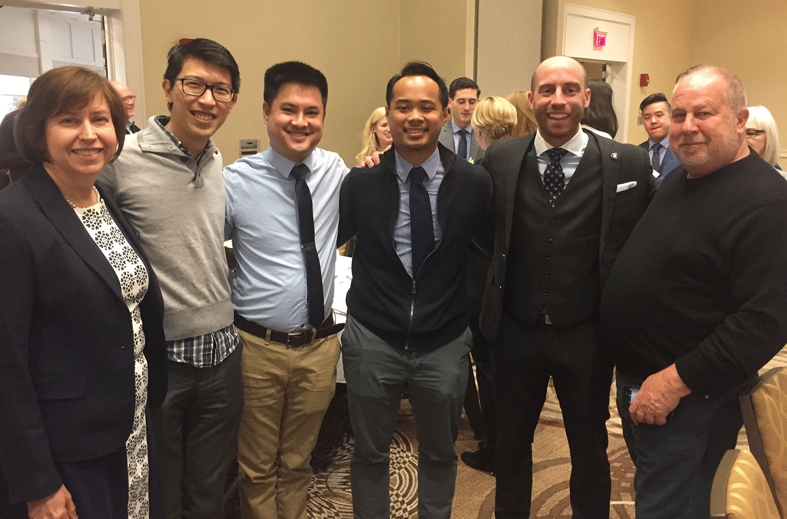 Penn State College of Medicine MD/PhD Medical Scientist Training Program co-directors Leslie Parent, MD (left), and Robert Levenson, PhD (right), are seen with four of the five program students who matched with residencies during the March 2018 Match Day celebration. The students are, from left, Paul Hsu, Jeffrey Nguyen, Ron Panganiban and Francis LeBlanc. Nicholas Sterling, who also matched, is not pictured. The six people are seen standing in a line in a crowded room, smiling, wearing dress clothes, with their arms around each other.