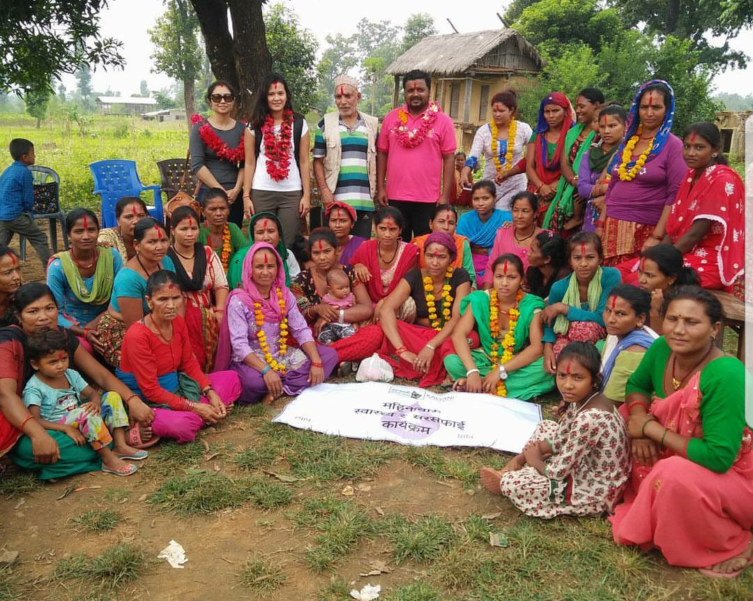 Penn State College of Medicine student Aditi Sharma, standing in the back row, second from left, and wearing a white top, is seen with community members in midwest Nepal. Sharma is pictured with dozens of men, women and children standing and seated in front of her. A small building is visible in the background.