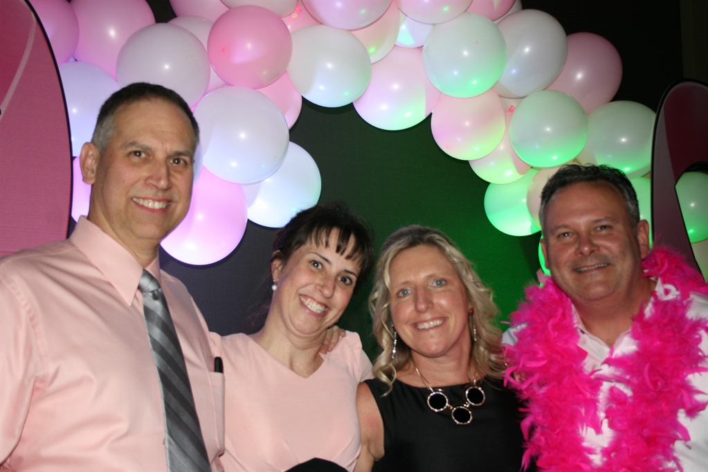 Four people are picutred wearing shades of pink and black at a breast cancer fundraiser party thrown by survivor Kathy, who is pictured third from left. An arch of pink and white balloons is visible behind the people pictured.