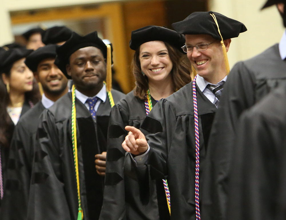 Ben Abney acknowledges someone in the audience as he joins his fellow graduates while entering the 48th commencement for Penn State College of Medicine, held May 20, 2018, at the Hershey Lodge. Abney is pictured smiling and pointing, and a row of other students is visible behind him.