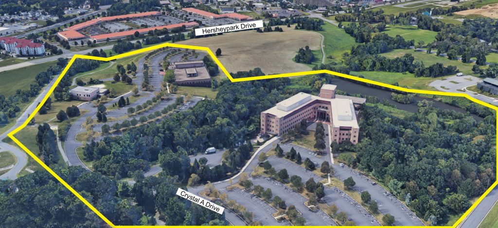 An aerial view of the Crystal A Drive buildings. Three buildings as well as parking lots and patches of trees are within a bright yellow line drawn on the image.